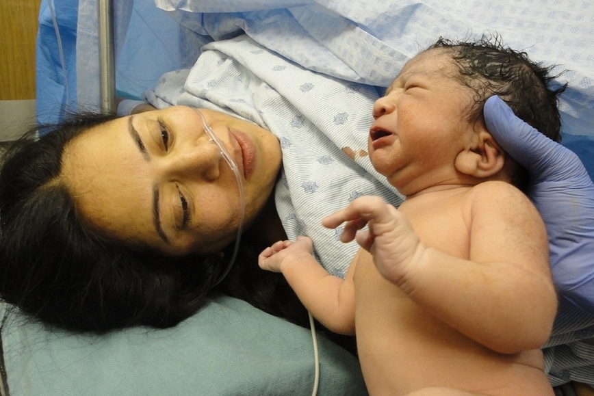 Kobieta bezpośrednio po porodzie, obok jej nowo narodzone dziecko.