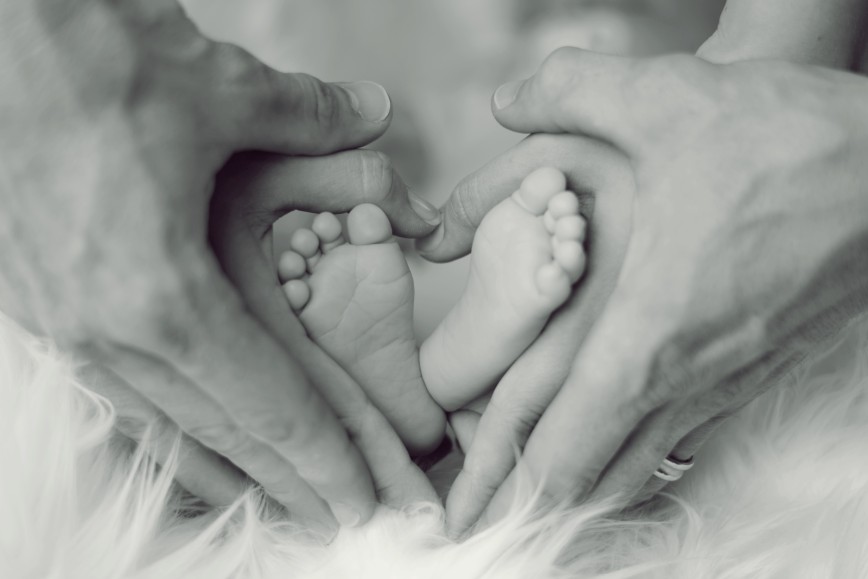 Stopki noworodka i dłonie rodziców splecione na kształt serca.