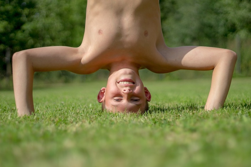 Na zdjęciu młody chłopak stoi na głowie bezpośrenio na trawie