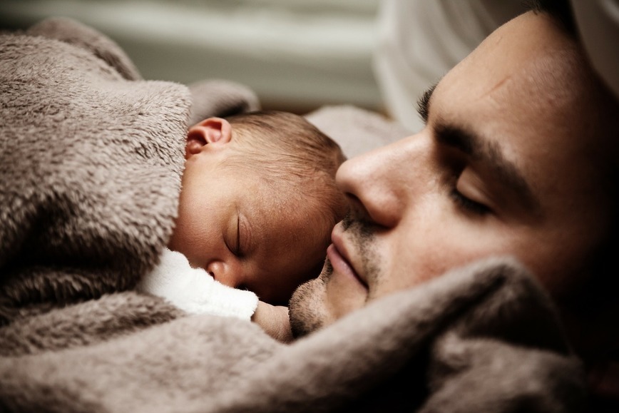 na zdjęciu ojciec śpi z noworodkiem na swojej piersi