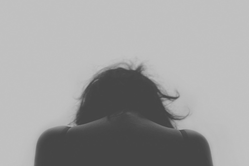 zdjęcie w kolorystyce czarno białej przedstawia kobietę ze skuloną głową, jest wykonane od tyłu