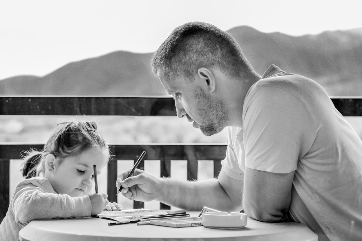 Zdjęcie przedstawia mężczyznę z dzieckiem, które rysuje. Zdjęcie wykonano w kolorystyce czarno białej.