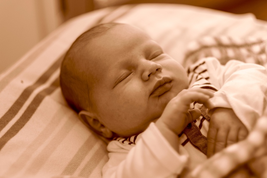 zdjęcie w kolorystyce sepii, przedstawia śpiącego noworodka